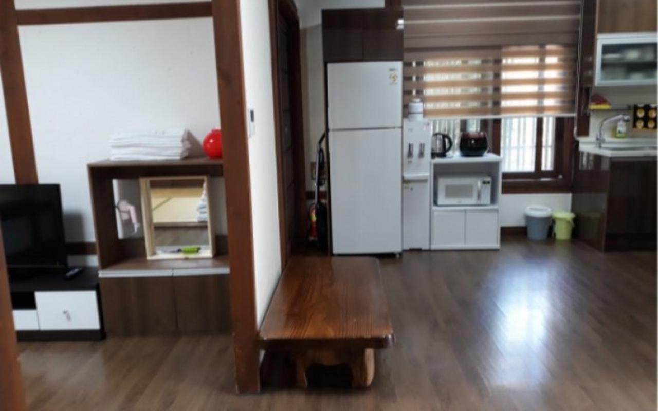 낮은 탁자와 TV 수납장, 냉장고와 주방 가전이 배치된 실내입니다.