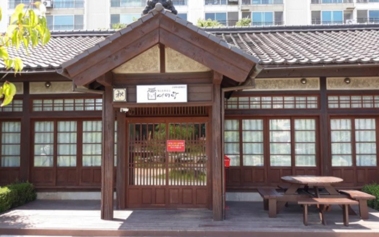 처마 아래 가을 추 문패와 데크 위 야외 목재 테이블이 놓인 한옥 외관입니다.